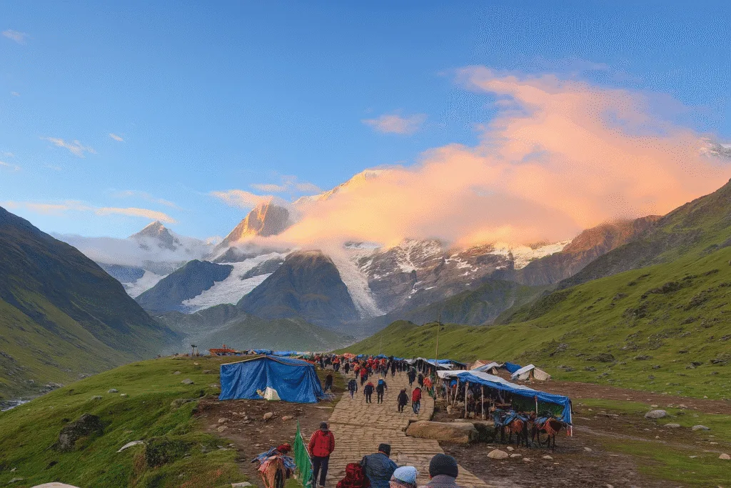 Pilgrims walking on a stone-paved path near Linchauli on the Kedarnath trek route, surrounded by lush green hills, blue tents, and snow-covered Himalayan peaks under a clear blue sky with orange clouds during sunrise.